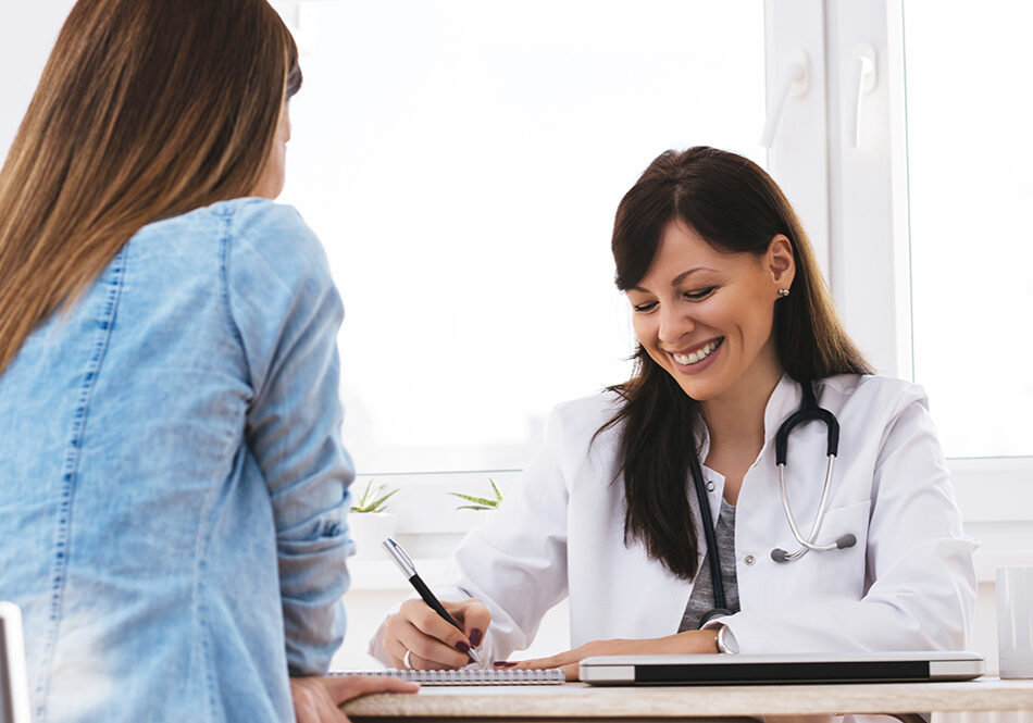 Smiling doctor having a funny conversation with patient. Beautiful female doctor writing report and smiling.