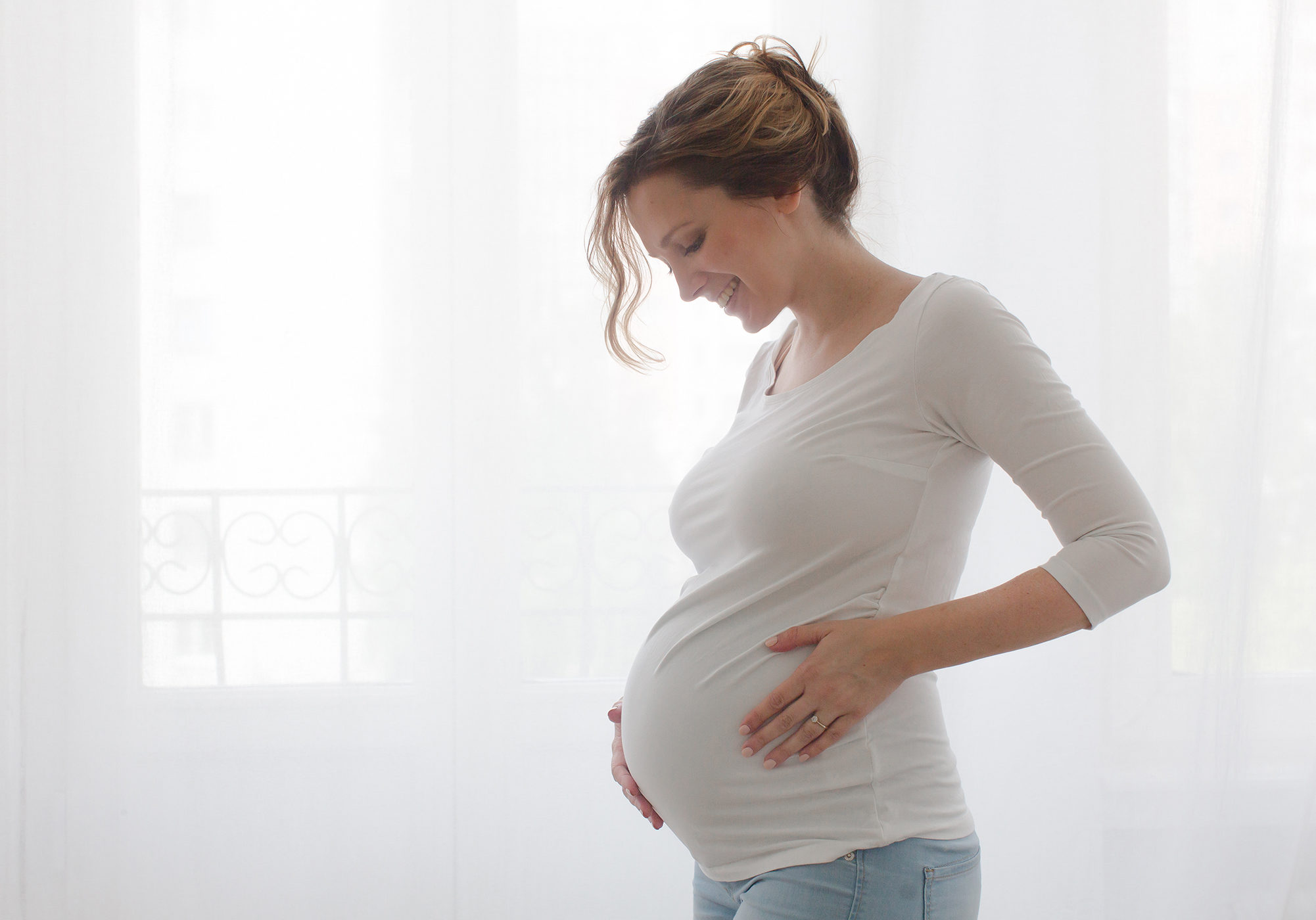 Young pregnant woman with eyes closed embracing her stomach. Horizontal indoors shot.